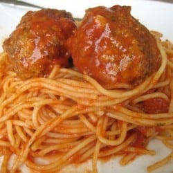 Spaghetti noodles topped with marinara sauce and 2 meatballs on a white plate.