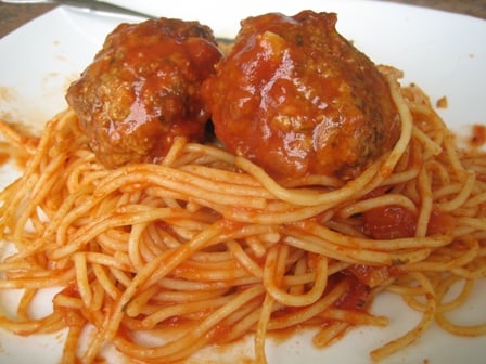 Spaghetti noodles topped with marinara sauce and 2 meatballs on a white plate.