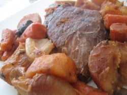 Pot roast with cooked potatoes, carrots, onions, and mushrooms on a plate.
