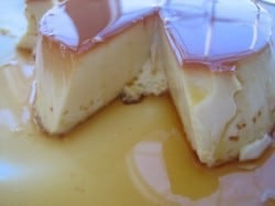 Flan on a plate toped with caramel with a slice removed showing the interior texture.