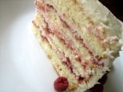 A slice of layer cake with raspberry preserves and cream cheese frosting sandwiched between 4 cake layers on a white plate.