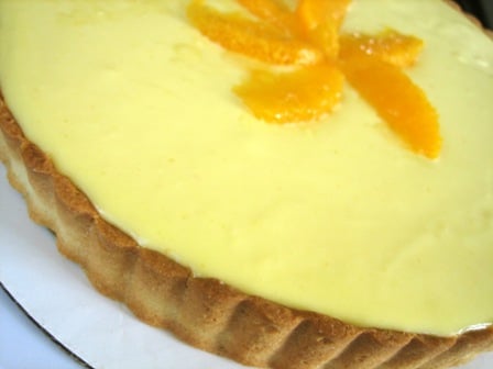 Orange cream tart before slicing on a white plate.