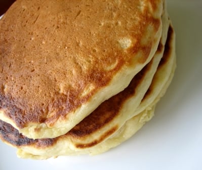 Overhead image of a stack of 3 buttermilk pancakes on a white plate.