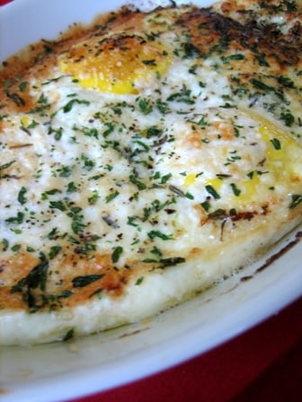 Baked eggs topped with herbs and cheese on a plate with a spoon.