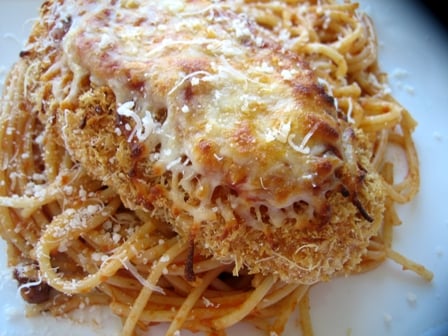 Chicken parmesan on top of noodles on a white plate.
