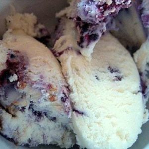 Scoops of blueberry cheesecake ice cream in a white bowl.