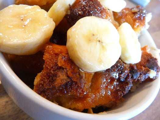 Bread pudding with banana slices in a white mug.