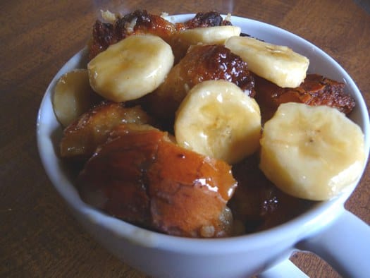 Bread pudding with banana slices in a white mug.