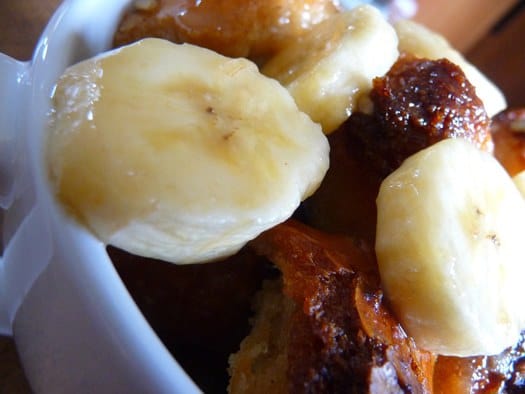 Bread pudding with banana slices in a white mug.