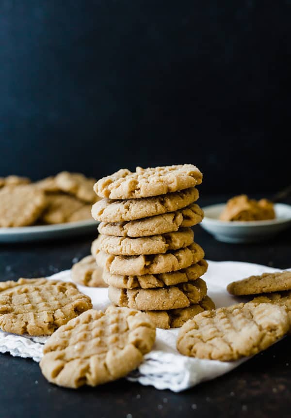 A stack of peanut butter cookies with additional cookies on a napkin.