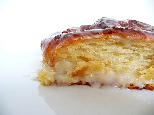 Side view of a cheese cinnamon roll on a white plate.