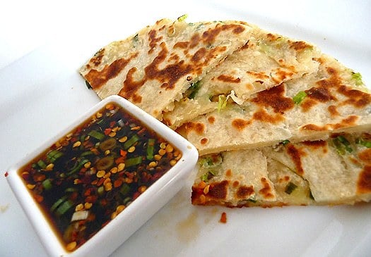 Scallion pancakes with a ginger dipping sauce on a white plate.