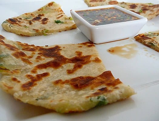 Scallion pancakes with a ginger dipping sauce on a white plate.
