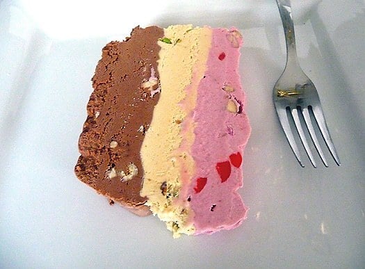 Slice of spumoni ice cream terrine on a white plate with a fork.