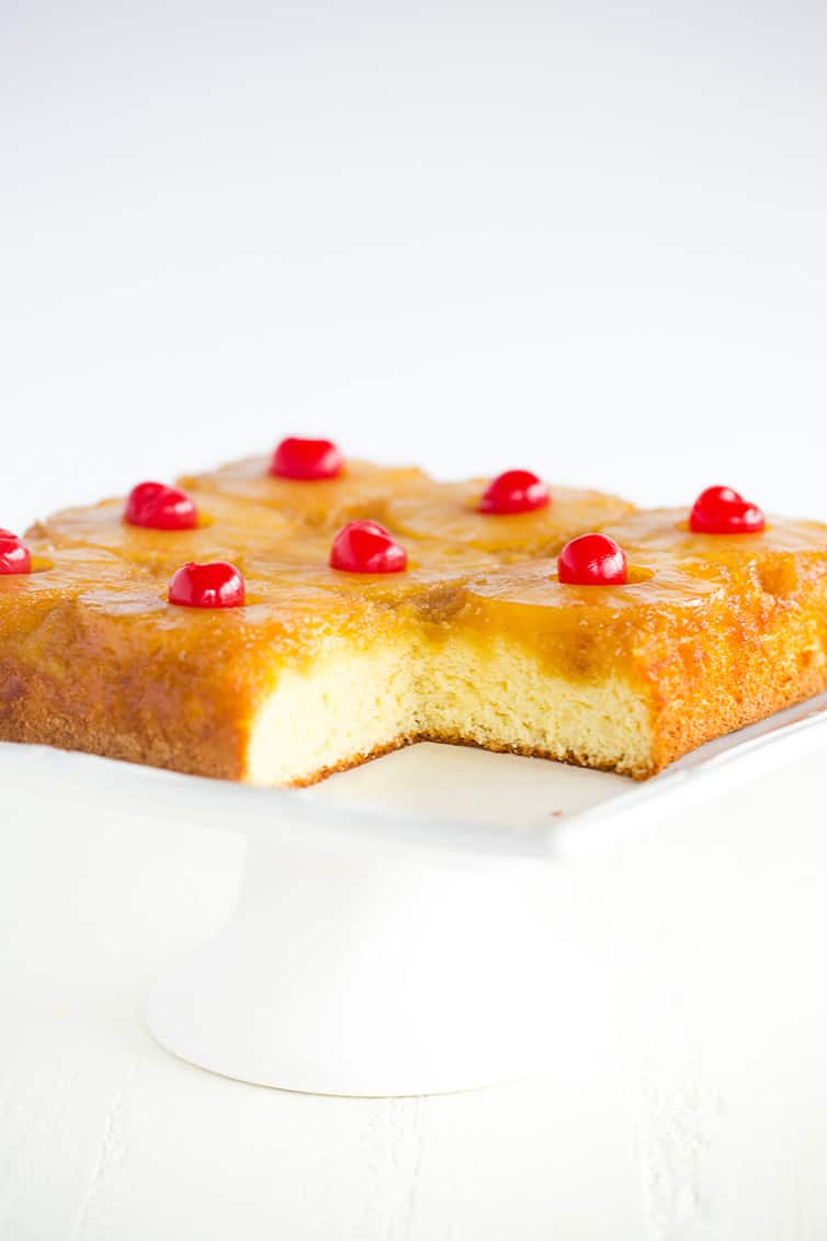 A pineapple upside down cake on white platter with a corner piece removed.