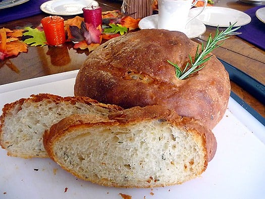 2 slices of potato rosemary bread with the full loaf of bread on a cutting board.