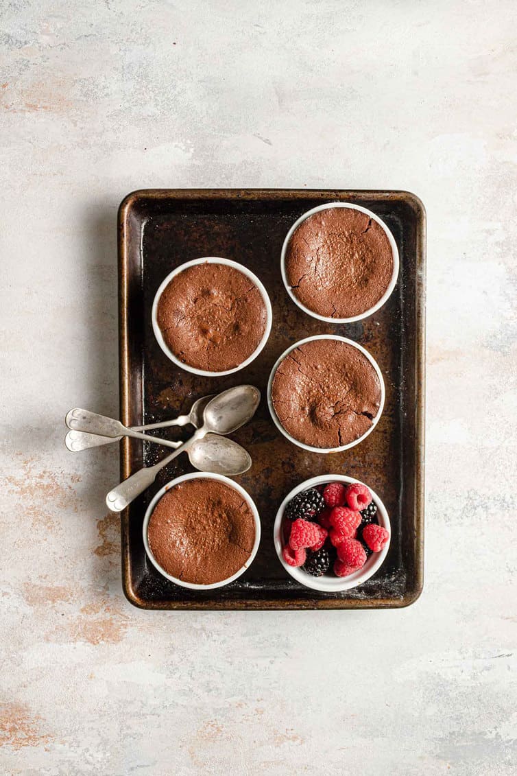 A baking sheet with four ramekins of baked chocolate lava cakes.