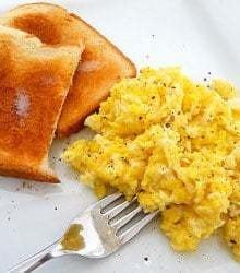 Scrambled eggs with 2 pieces of toast on a white plate with a fork.