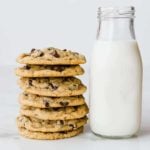 A stack of peanut butter-oatmeal chocolate chip cookies next to a glass bottle of milk.