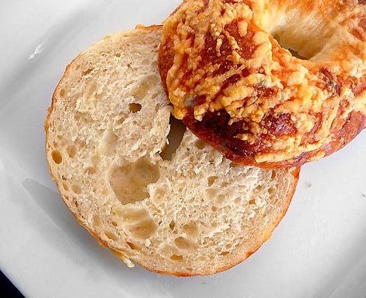 Asiago bagel cut in half on a white plate.