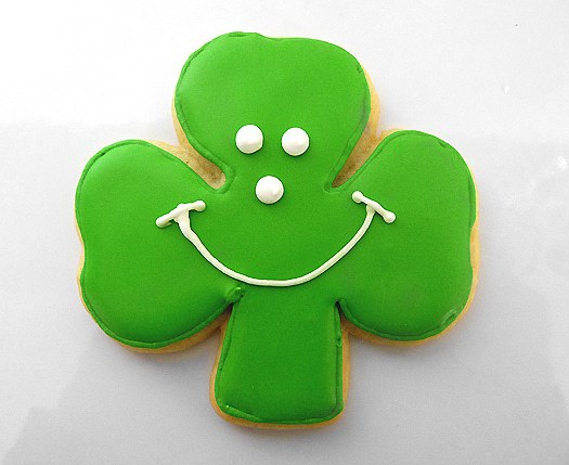 Shamrock sugar cookie with green icing and a white smiley face.