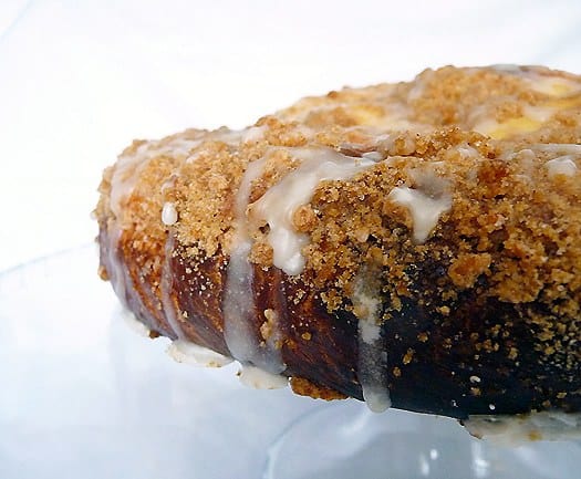 Side view of coffee cake with sweet cheese filling and vanilla icing on a glass cake stand.