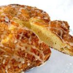 Coffee cake with icing on a glass serving platter with a slice removed.