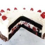 Black forest layer cake topped with frosting and cherries with a slice removed showing the inside.