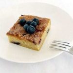 Square of blueberry butter cake topped with blueberries on a white plate with a fork.