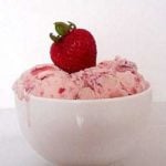 Scoops of strawberry ice cream in a white bowl topped with a fresh strawberry.
