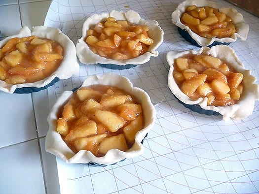 Peach pie filling on top of pie crust in 5 mini pie dishes before baking.
