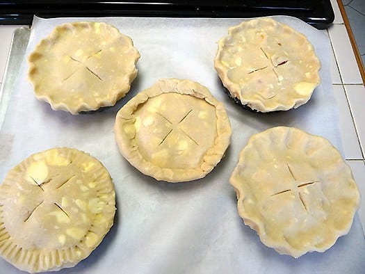 5 peach pie tartlets on a parchment paper lined baking sheet before baking.