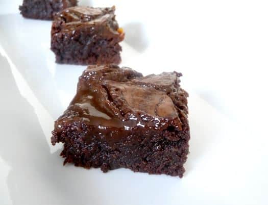 Squares of salted caramel brownies on a white plate.