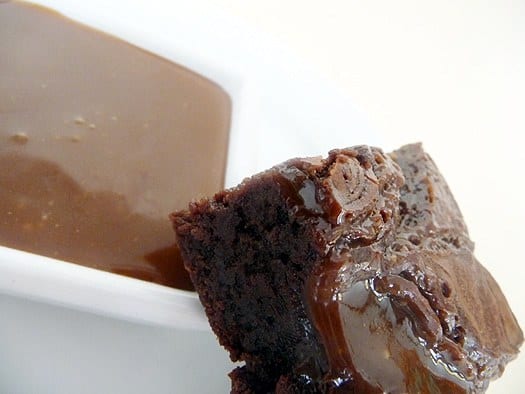 Close up image of a salted caramel brownie next to caramel sauce in a white bowl.
