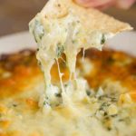 Dipping a tortilla chip into a pan of spinach artichoke dip.