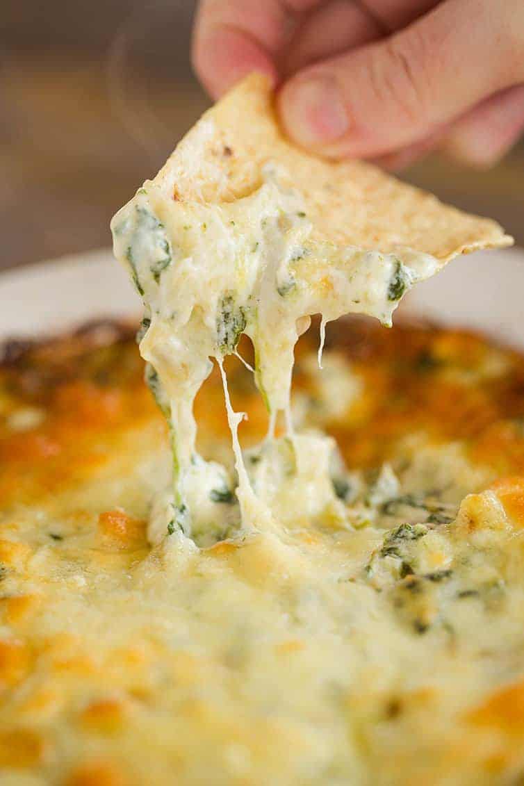 Dipping a tortilla chip into a pan of spinach artichoke dip.