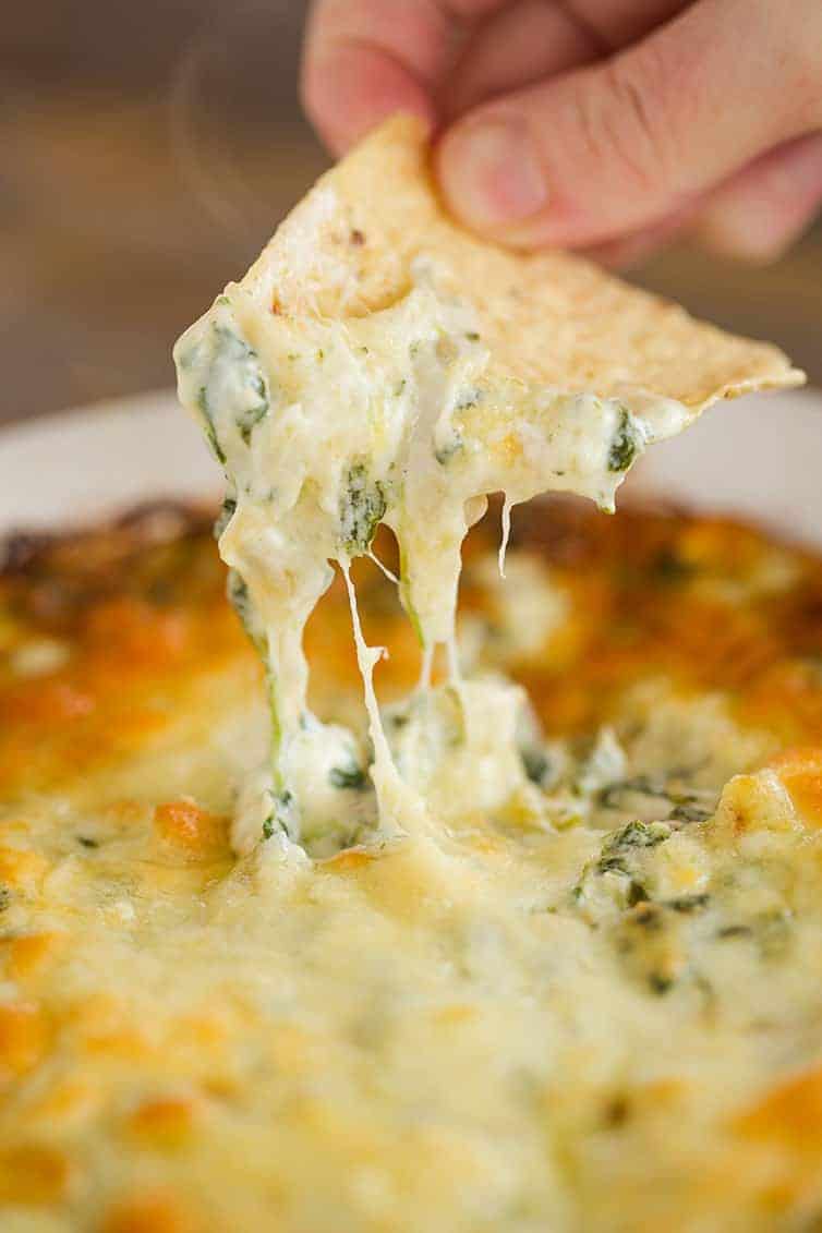Dipping a tortilla chip into a pan of spinach artichoke dip.
