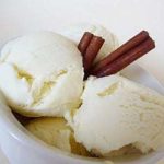 Scoops of cinnamon ice cream in a white bowl garnished with cinnamon sticks.