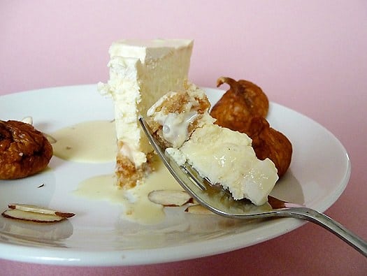 Forkful of fig and almond cheesecake on a white plate with a slice of cheesecake on it.