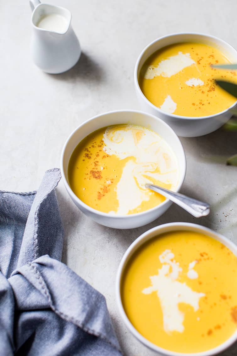 Three bowls of butternut squash soup with a side of cream.