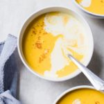 Three bowls of butternut squash soup with a drizzle of cream and pinch of nutmeg.
