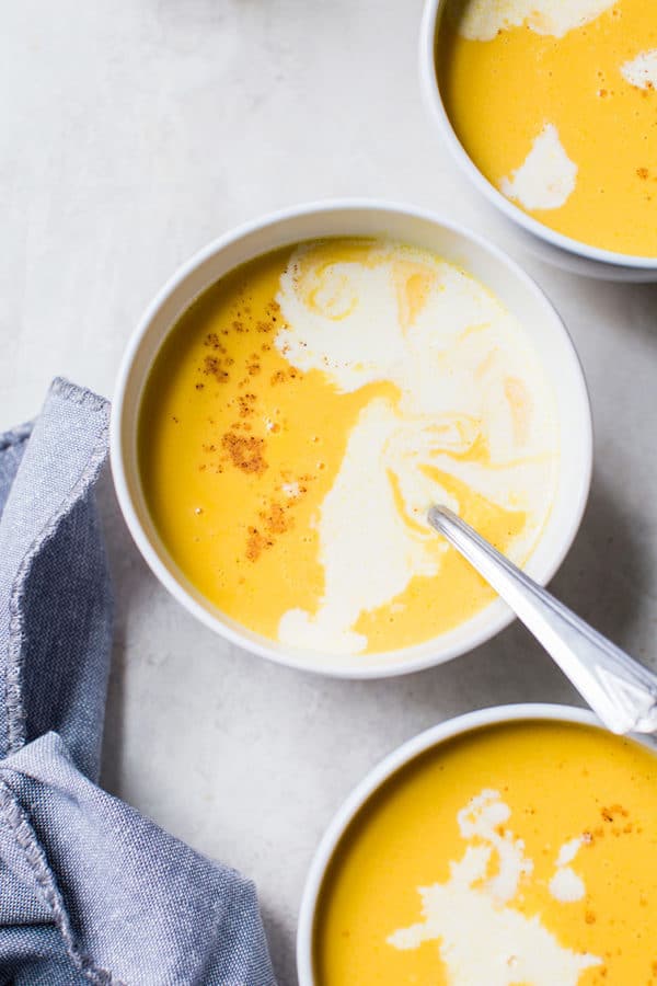 Three bowls of butternut squash soup with a drizzle of cream and pinch of nutmeg.
