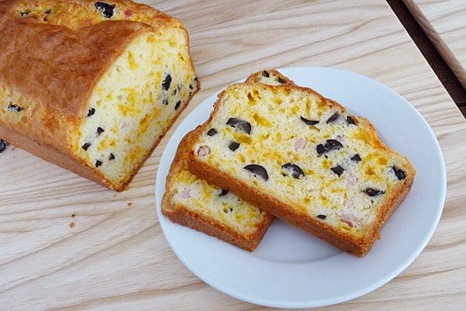 Loaf of cheese, olive, and ham bread with 2 slices of the bread on a white plate.