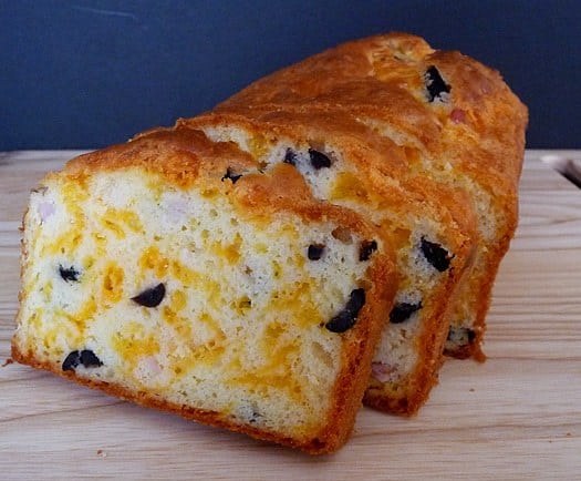 Sliced loaf of cheese, olive, and ham bread on a wood cutting board.