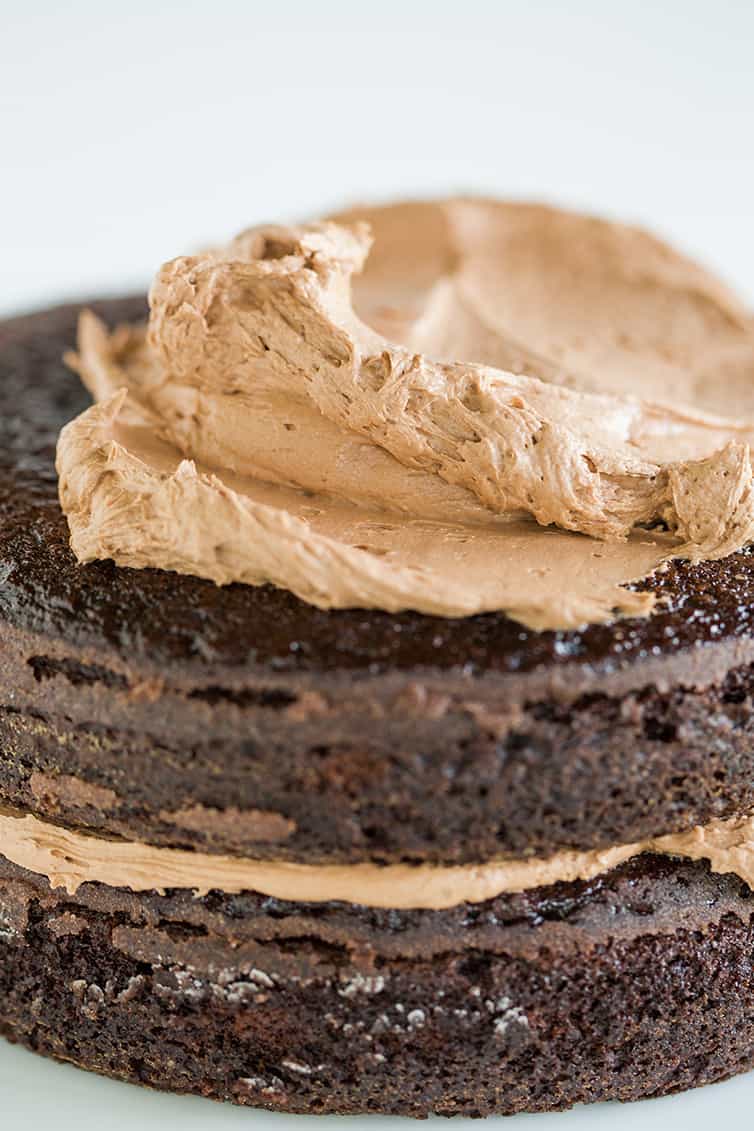 Chocolate cake being frosted with chocolate frosting.