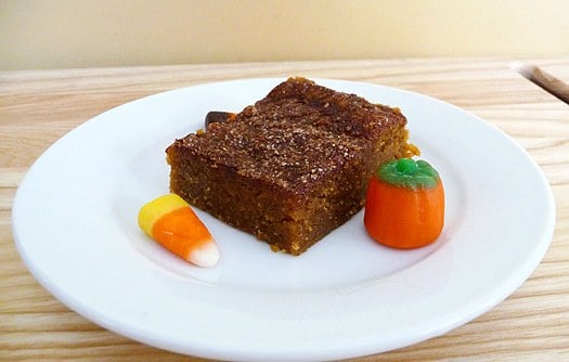 Square of pumpkin pie bars on a white plate with candy corn garnish.