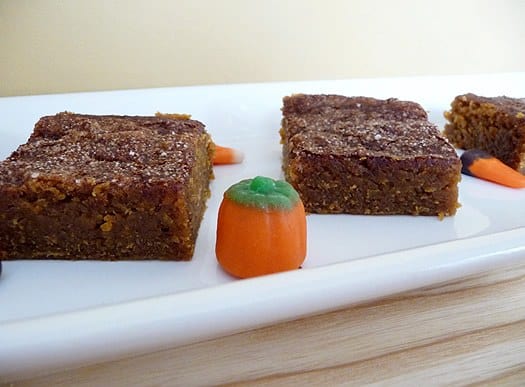 Squares of pumpkin pie bars on a white serving plate with candy corn garnish.