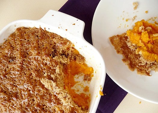 Overhead image of mashed sweet potato brûlée in a casserole dish with a serving scooped out onto a white plate showing the inside texture.