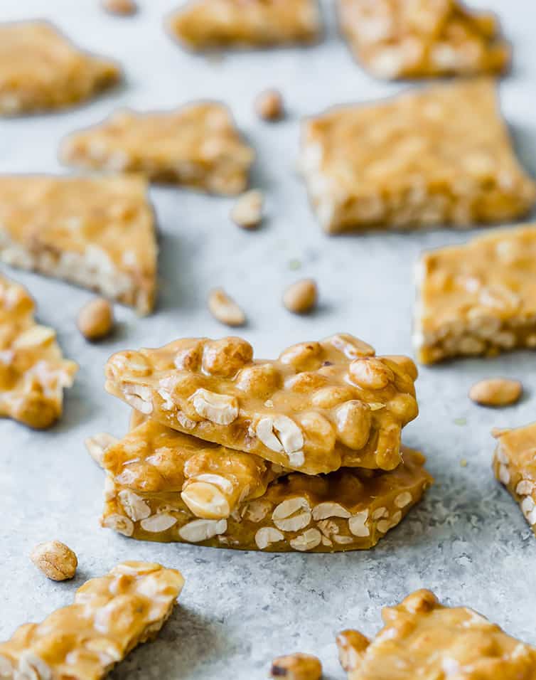 Three pieces of peanut brittle stacked, among broken pieces of peanut brittle.