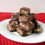 Squares of chocolate walnut fudge stacked on a white plate.